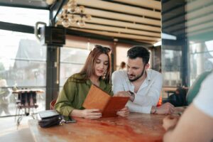 a man and woman sitting at a table looking at a menu