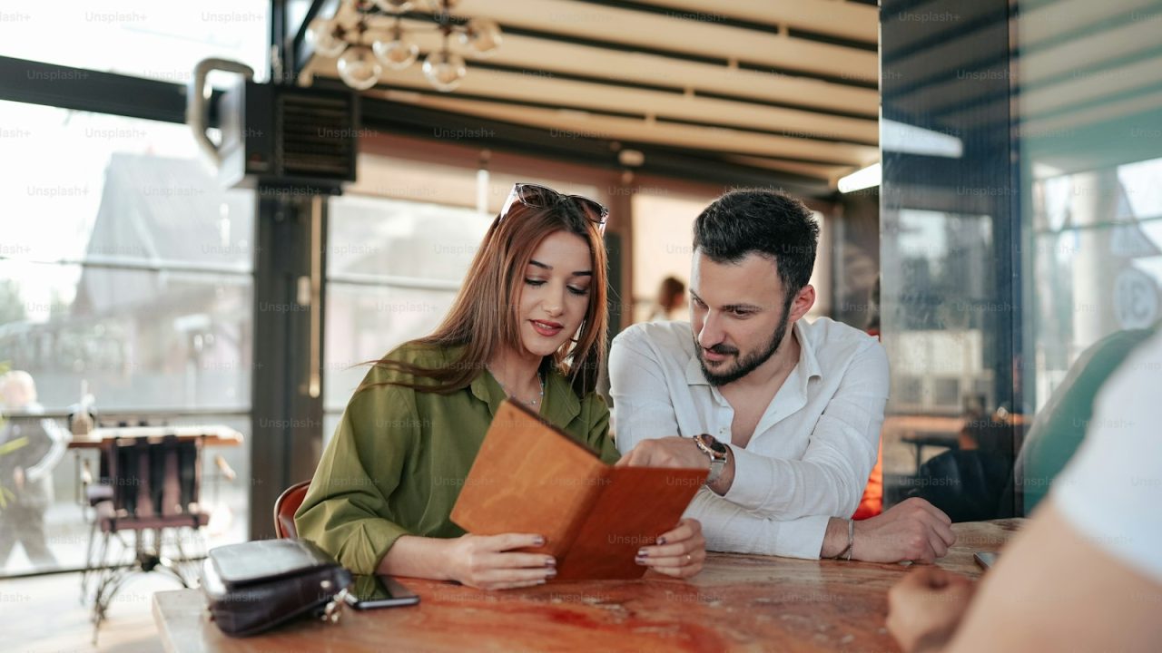 a man and woman sitting at a table looking at a menu