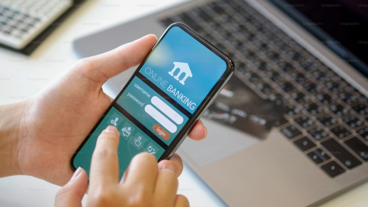 Mobile banking. Man holding smartphone showing online bank application on screen at desk workspace in office. e-banking