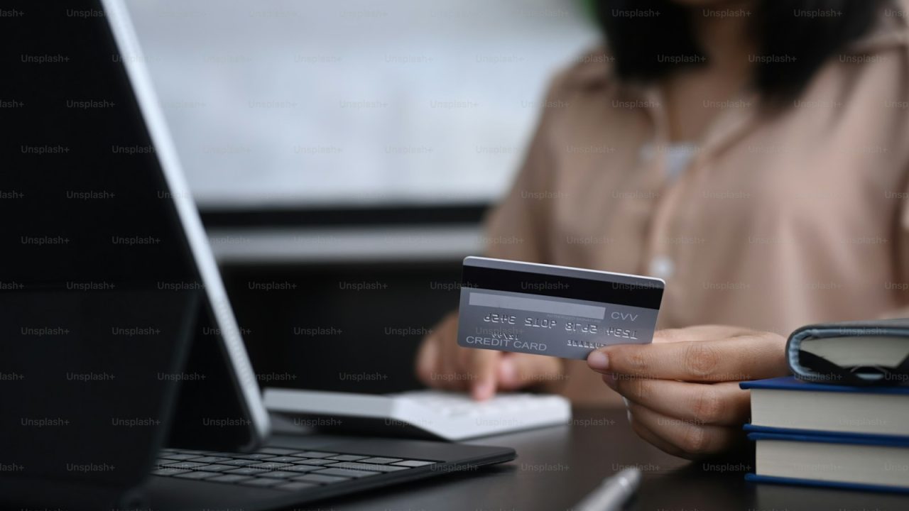 Young woman holding credit card and making calculations for online shopping or online payment.
