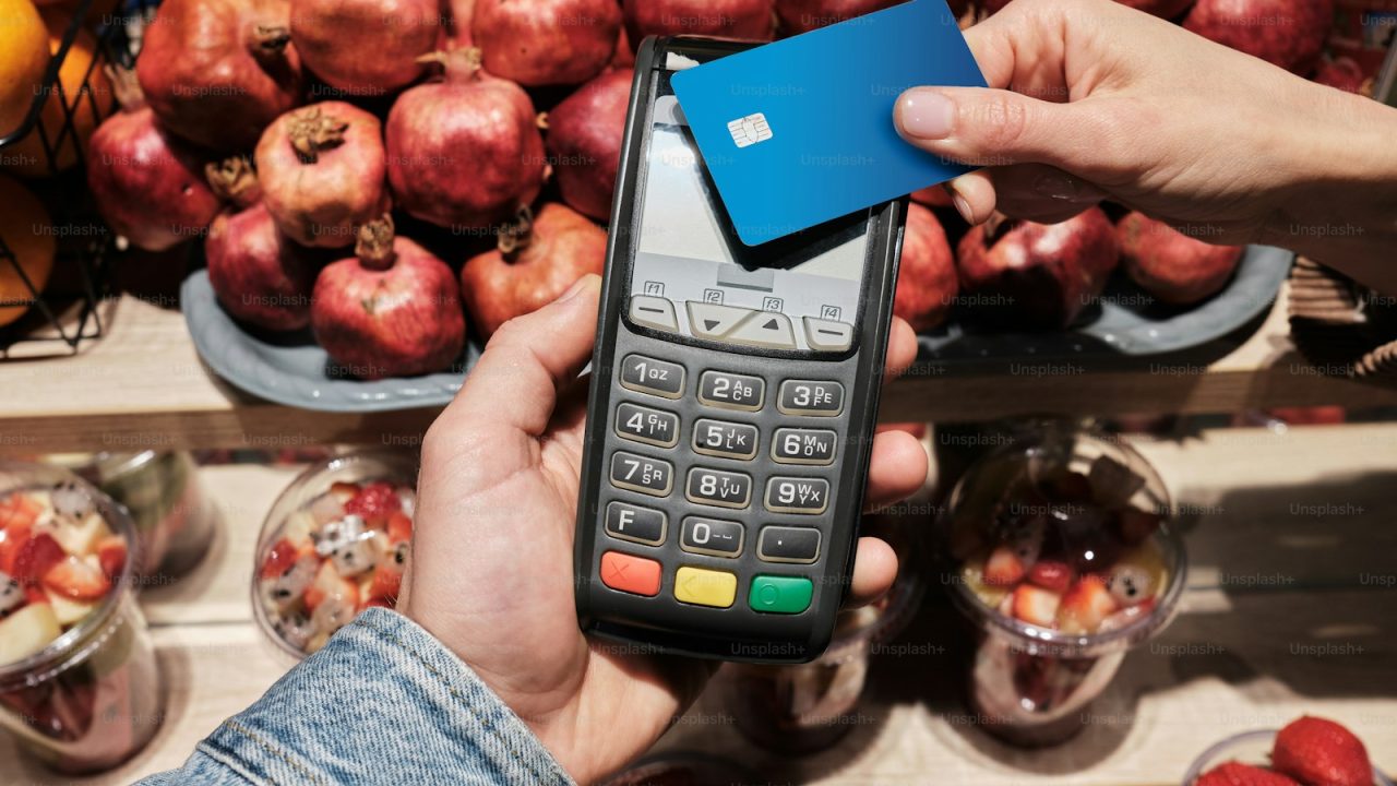 a person holding a cell phone in front of a pile of fruit