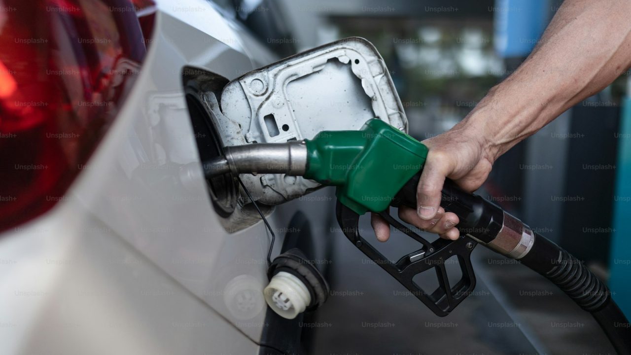 A close-up of worker standing on gas station and fueling car.