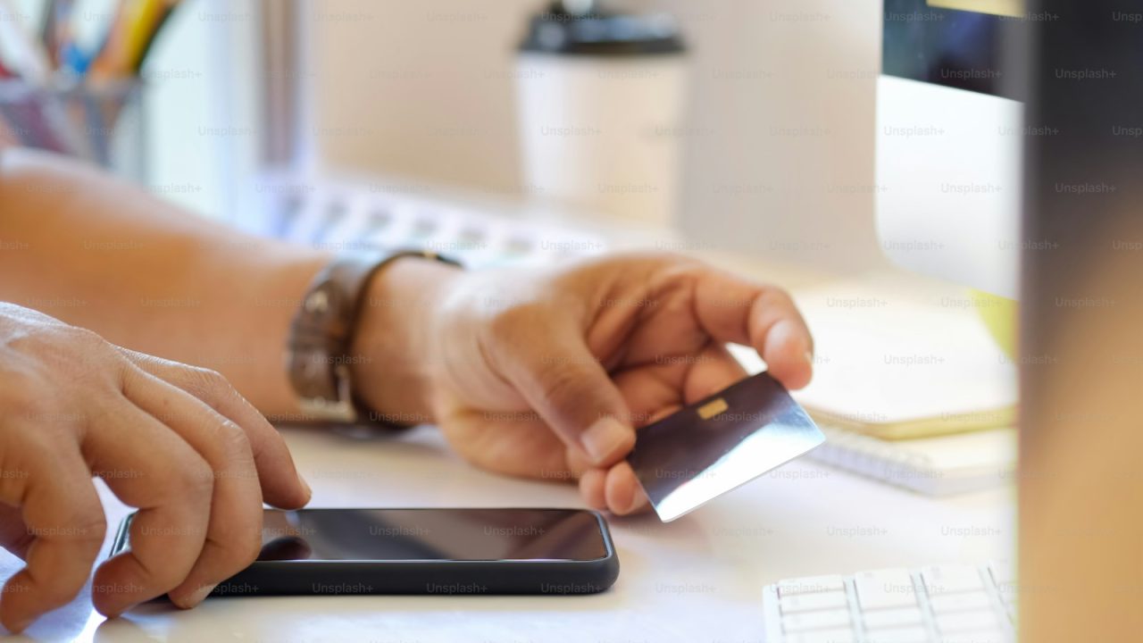 Online payment Concept. Man using credit card with mobile phone and coffee cup on white office desk.