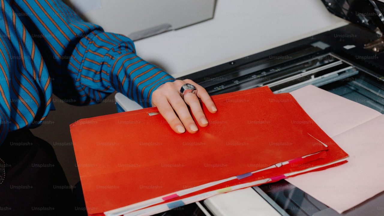 a person holding a binder in front of a printer